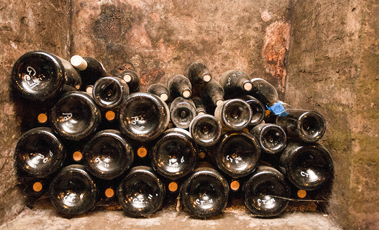 Old and dusty wine bottles stacked up in a concrete basement