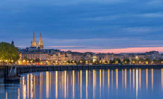 Evening shot of Bordeaux with a large church in the background and all the city lights reflecting off the river