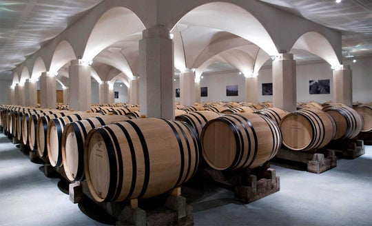 Large white room with arches, with rows of barrels with wine aging inside at Domaine Henri Boillot