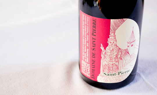 Close up of a bottle label for Domaine de Saint Pierre, red label with a church and priest on the front